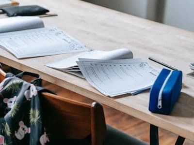 Student table with opened copybooks papers and backpack left on chair in contemporary school classroom