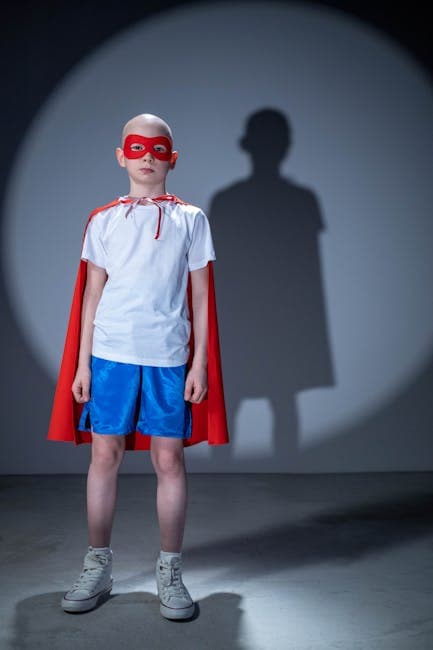 A child dressed as a superhero, wearing a red cape and mask, standing in spotlight shadow.